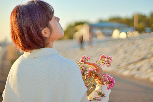花を手に持ち空を見上げる女性